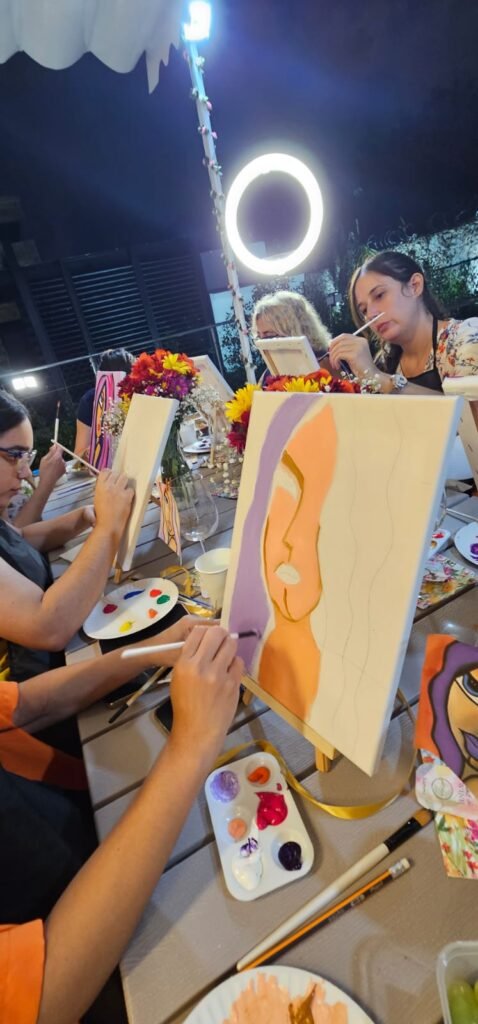 Una participante mezcla color en su paleta frente al lienzo, en una sesión nocturna de Aloeve