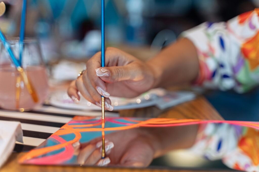 A close-up of a hand painting abstract designs on a mirror surface with a paintbrush.